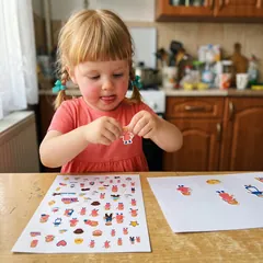 O fetiță dezlipește un sticker cu ea însăși la masa din bucătărie